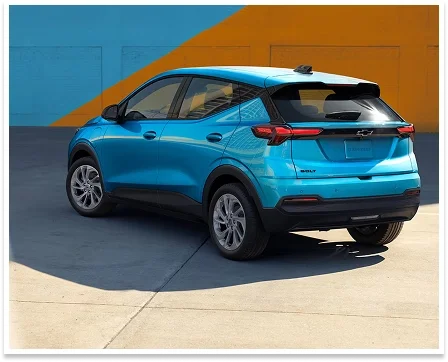 Rear three-quarter view of the 2027 Chevrolet Bolt in blue against a colorful orange and blue wall