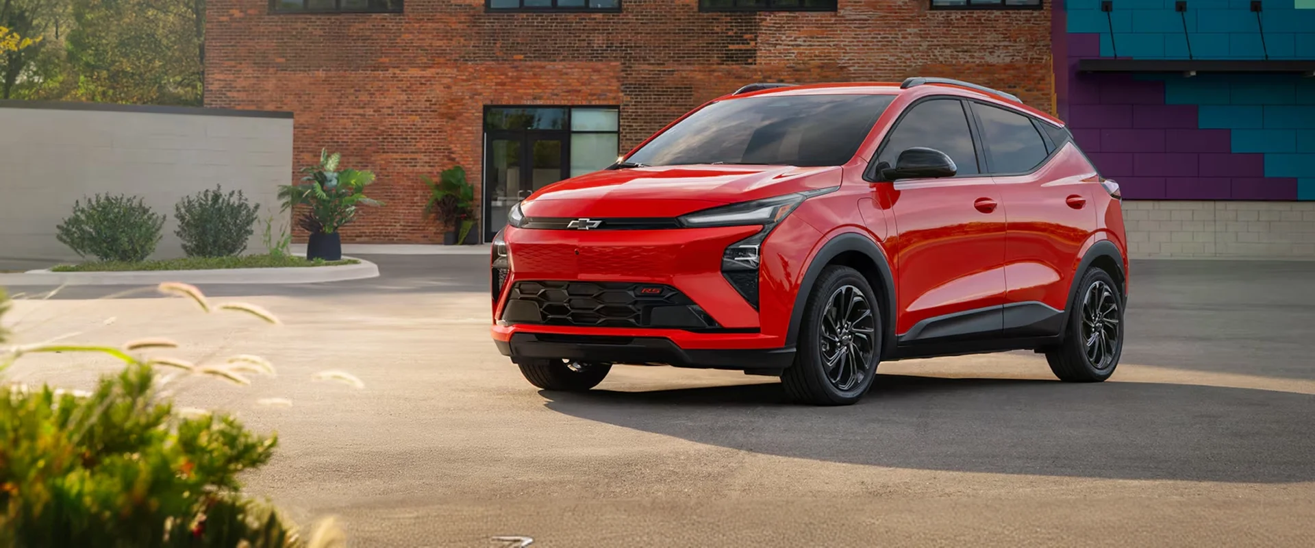 2027 Chevrolet Bolt EV in red driving through a scenic landscape with mountains in the background