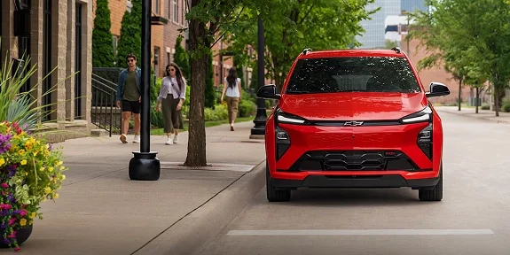 2027 Chevrolet Bolt RS in red viewed from the front on a tree-lined neighborhood street