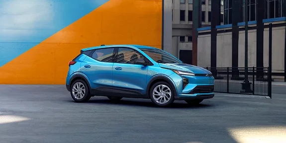 2027 Chevrolet Bolt LT in blue from a front three-quarter angle parked against a colorful building