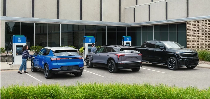 Multiple Chevrolet EVs including a blue Bolt charging together at a public station with a person nearby