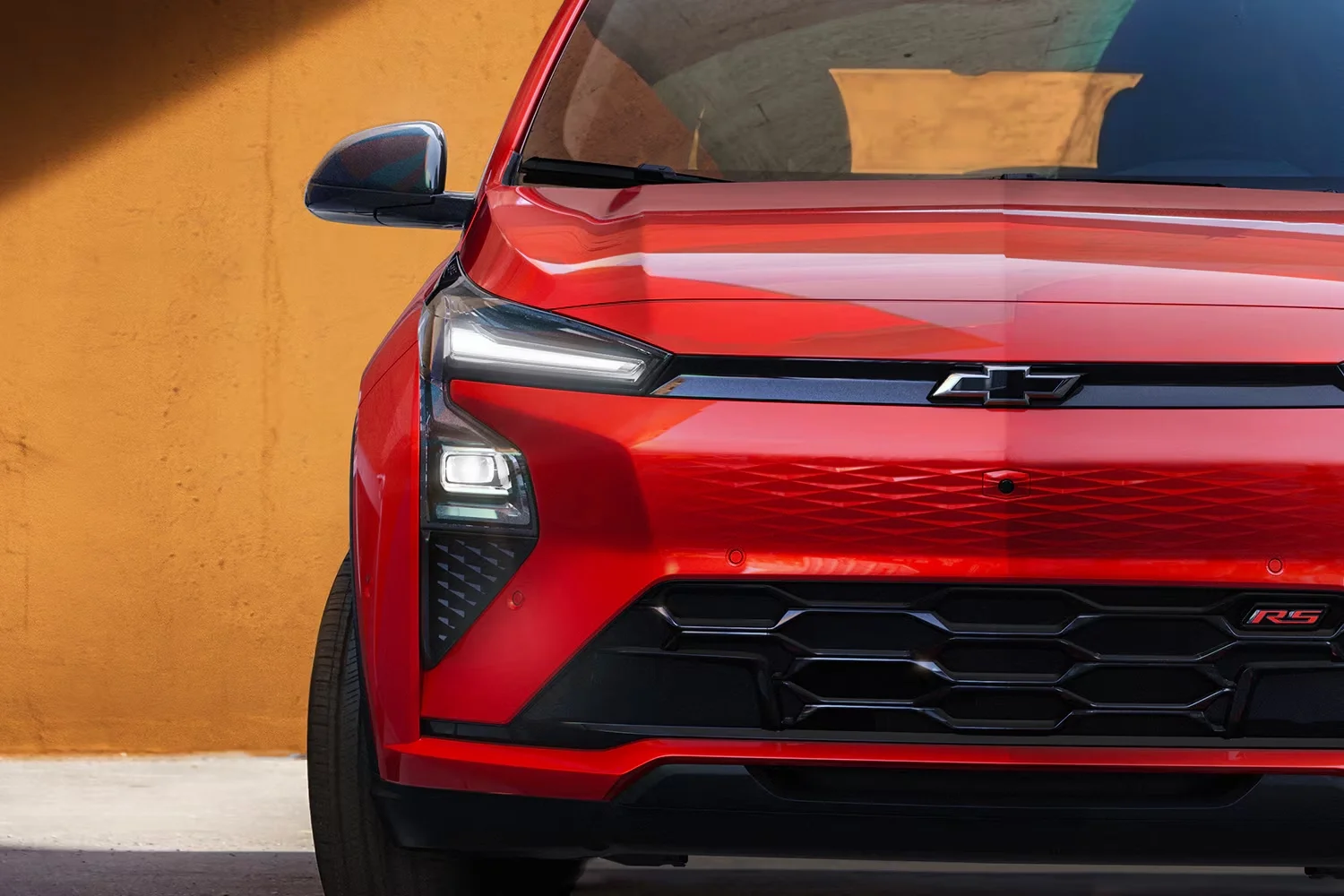 2027 Chevrolet Bolt RS in red parked on a city street, showcasing the sporty front grille and black roof rails